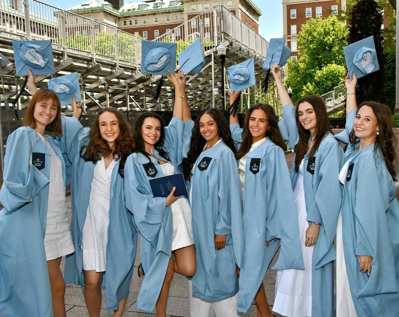 Graduating Students in robes, posing and holding their caps in the air.
